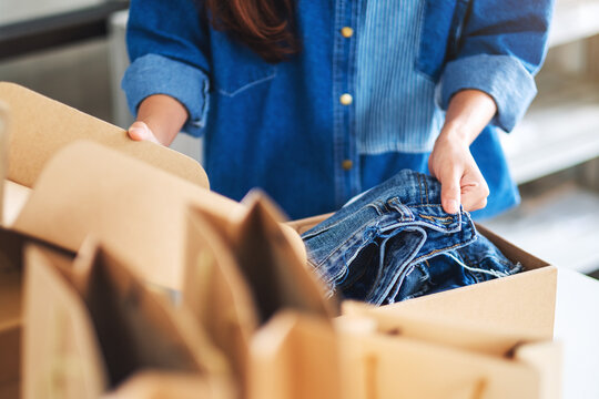 Closeup image of a woman receiving and opening a postal parcel box of clothing at home for delivery and online shopping concept
