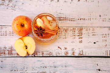 Crystal low glass of cider with anise and cinnamon on a wooden table, next to a whole and ripe ripe...