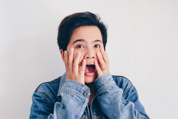 Short hair asian woman wear jeans jacket screams with joy and happiness, surprise feeling, winner expression, black shirt, white background. Indonesian women