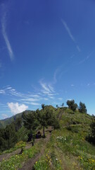 the view of a green hill with blue clouds and sky