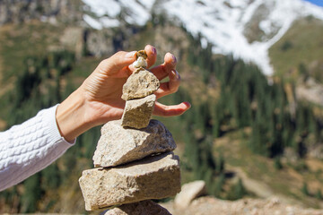 Cairn on the background of snowy mountains. Woman hand puts a stone