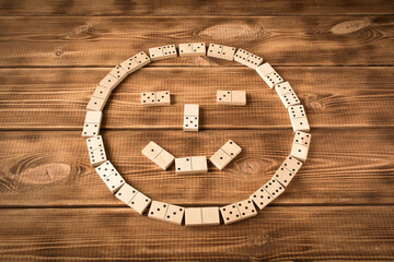 A game of dominoes. A smiley face made of Domino pieces on a wooden table.