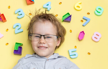 Little blond toddler child playing with lots of colorful plastic digits or numbers, indoor. Kid boy wearing colorful shirt and having fun with learning math