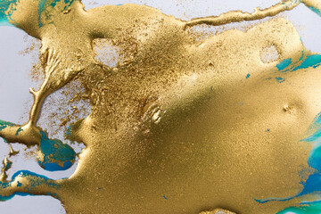 Gold and blue mixed inks splattered on white paper background.