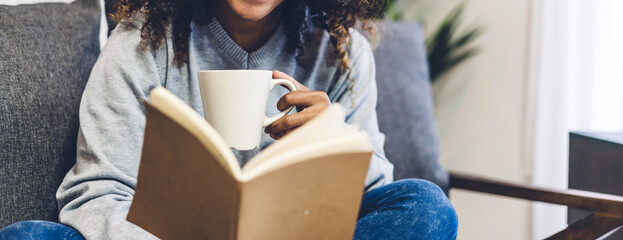 Young hipster african american black woman relaxing reading the paper book work study and looking at page magazine while sitting on couch at home