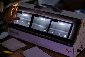 The inspector is reviewing to the radiography film of the pipe welds. The writes on the films are an penetrameter (European Standard). It is a quality indicators.