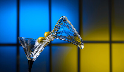 Martini and green olives in glass. Splashes on a colorful background.