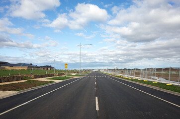 An asphalt road in a Melbourne's new suburb, with some modern residential houses on one side and...