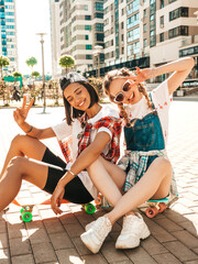 Two young smiling beautiful girls with colorful penny skateboards. Women in summer hipster clothes...