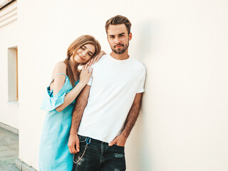 Fototapeta premium Portrait of smiling beautiful girl and her handsome boyfriend.Woman in casual summer jeans dress.Happy cheerful family.Female having fun.Couple posing in the street near white wall