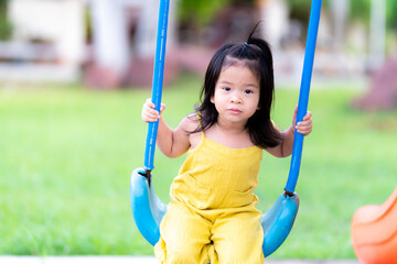 Active child having fun with swing chair at outdoor play area. Preschool kid happy back to play in playground at home. Portrait of adorable little girl sitting on swing in the playground on summer.