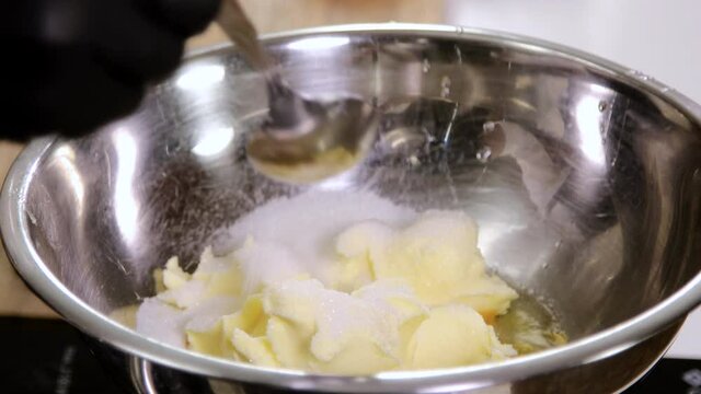 Close up of professional chef sprinkles three tablespoons of sugar over egg yolks and butter in a bowl. 4K
