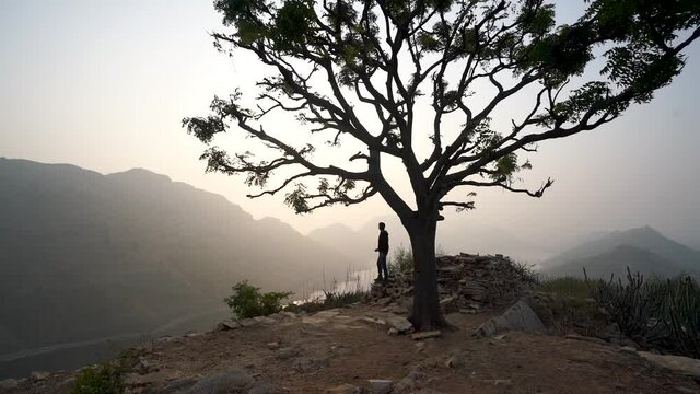 Silhouette Of A Man Standing Under The Tree Overlooking The Beautiful Lake Badi In Udaipur City, India On A Sunrise - wide shot