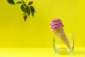 Homemade pink berry marshmallow in a waffle cone, in a transparent glass on a yellow background, with a sprig of grapes.