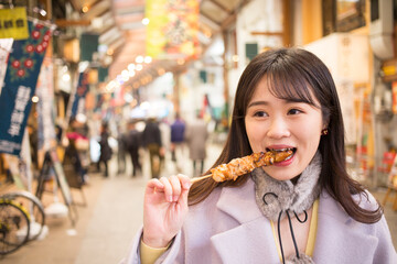 冬の商店街で焼き鳥を食べている可愛い若い女性