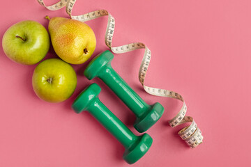 Fototapeta na wymiar Composition with dumbbells, twisted measuring tape and green apples on a pink background, top view. Concept of diet and healthy lifestyle