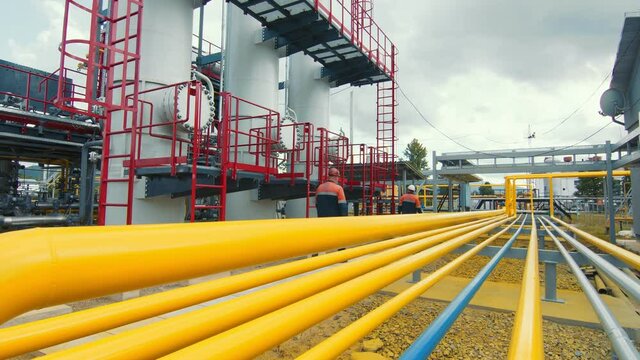 Gasman in a protective mask who walks along the gas production station and inspects it. Yellow gas distribution lines along which the gas flow is distributed.
