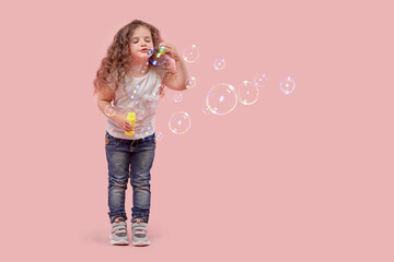 Cute girl with long curly hair blows soap bubbles. The baby is blonde.