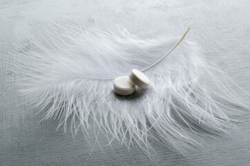 Closeup of drugs for sleep and white feather on the grey surface