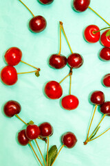 Cherry berries on a turquoise background, top view. The pattern is made from fresh berries