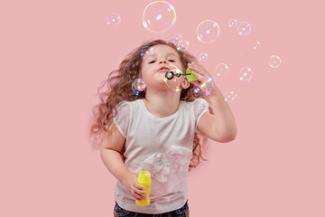 Cute girl with long curly hair blows soap bubbles. The baby is blonde.