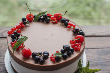 Mousse cake with berries on a wooden table. Chocolate cream cake with currants and cherries. Berry cake for birthday, wedding and other holidays.