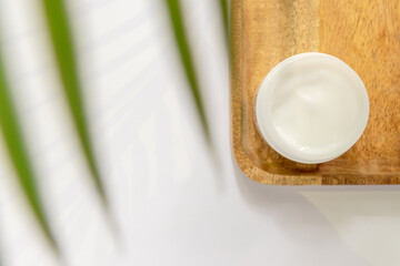 White jar of face cream on a wooden tray. white background, top view, tropical leaves. Concept of natural cosmetics and spa.
