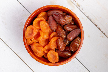 Dried apricots and dates in a wooden bowl with dates, flat lay