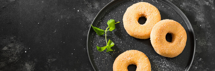 Doughnuts in sugar on a black plate on the black kitchen table. Lots of doughnuts on the plate. Top...