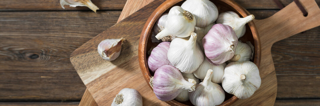 Garlic in a wooden bowl on a wooden table. lots of garlic in a bowl. Garlic close-up. Banner with space for text