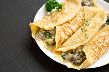 Savory Homemade Mushroom, Spinach and Cheese Crepes on a white plate on a black background, side view. Copy space.
