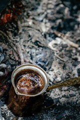 Boiling coffee in turkish cezva on campfire coals. Luxury camping concept.