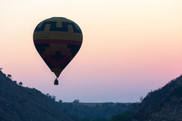 One hot air balloon floating over hills into an orange sunset
