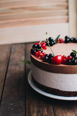 Mousse cake with berries on a wooden table. Chocolate cream cake with currants and cherries. Berry cake for birthday, wedding and other holidays.