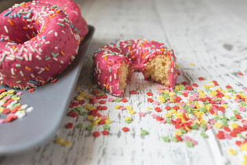 Obraz na płótnie Canvas a pink donut bitten in the foreground on a rustic wooden table and colored stars and two more pink donuts on a blue plate