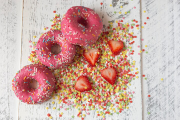 pink donuts on a rustic wooden table with strawberries and decorative stars around
