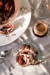 Glass bowl and plate with tiramisu dessert on white kitchen table.