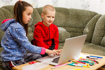 Two beautiful cute happy smiling children, a boy and a girl, use laptop for distance learning or entertainment.