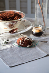 Glass bowl and plate with tiramisu dessert on white kitchen table.