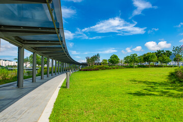 The glass walkways and lawns of the modern park in the city center are under the blue sky and white clouds.