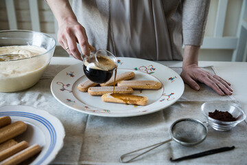Step by step tiramisu. Pouring coffee with cognac on ladyfingers.