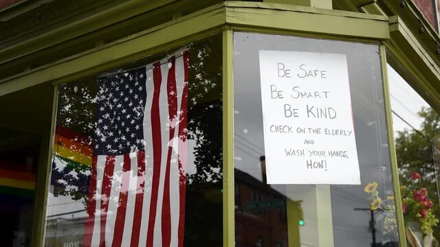 A glass store front displays American flag and sign that encourages kindness and looking after elderly.