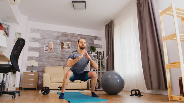 Athletic man training his legs doing squat exercise at home.