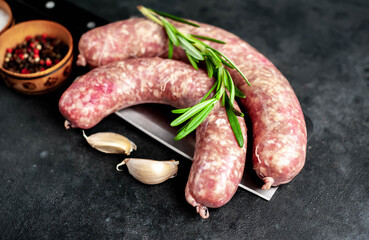raw sausages on a meat knife with spices and rosemary on a stone background