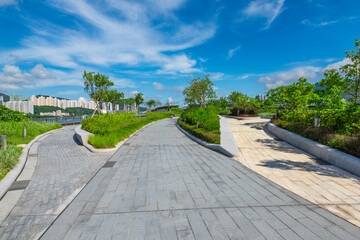 The pedestrian path in the central city park is under the blue sky and white clouds.