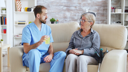 Male nurse sitting on couch with senior woman giving her medical treatment in nursing home.