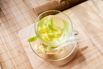 Transparent glass cup of herbal tea with linden flowers on a wooden background