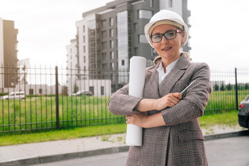 Stylish woman with glasses in uniform in a white helmet against the background of the business building.