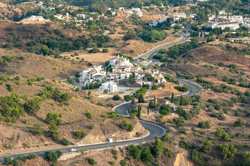 Fototapeta na wymiar bird's-eye view a winding road goes around a small settlement among the hills with greenery