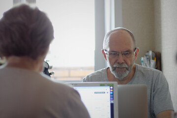 Senior man wearing eyeglasses typing on laptop keyboard while working at home, self isolation at home, remote work during quarantine